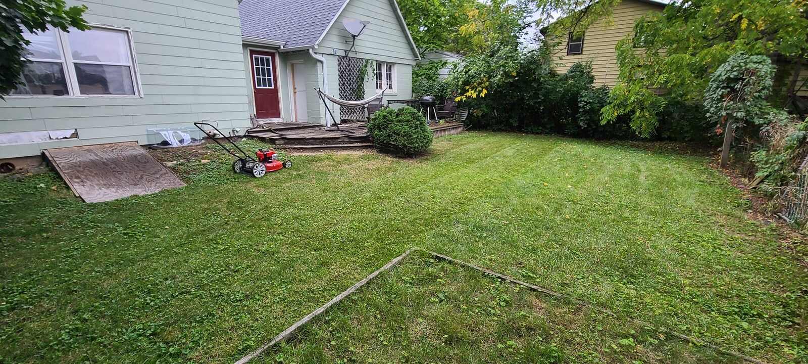 Freshly mowed backyard behind a green house with a patio and shrubs