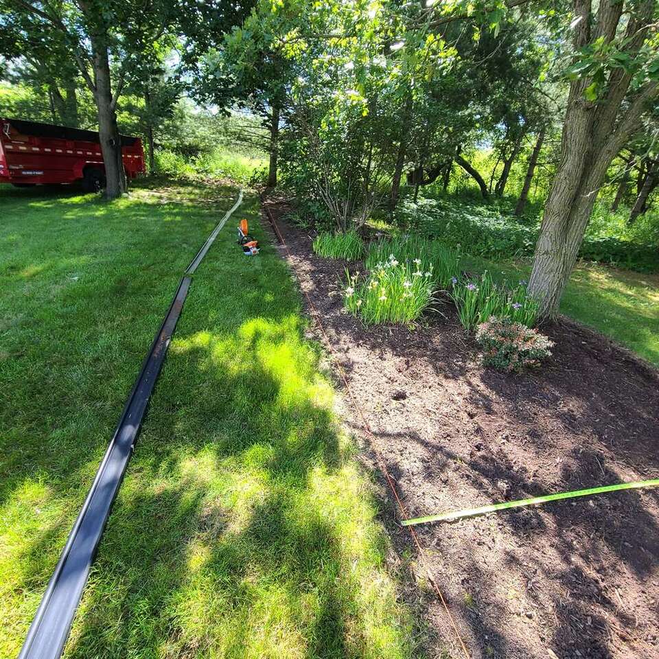 Shade garden bed with fresh soil and new edging being installed along a lawn
