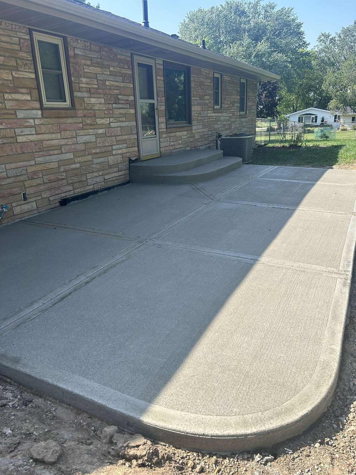 New concrete patio with a rounded corner and steps behind a stone ranch house