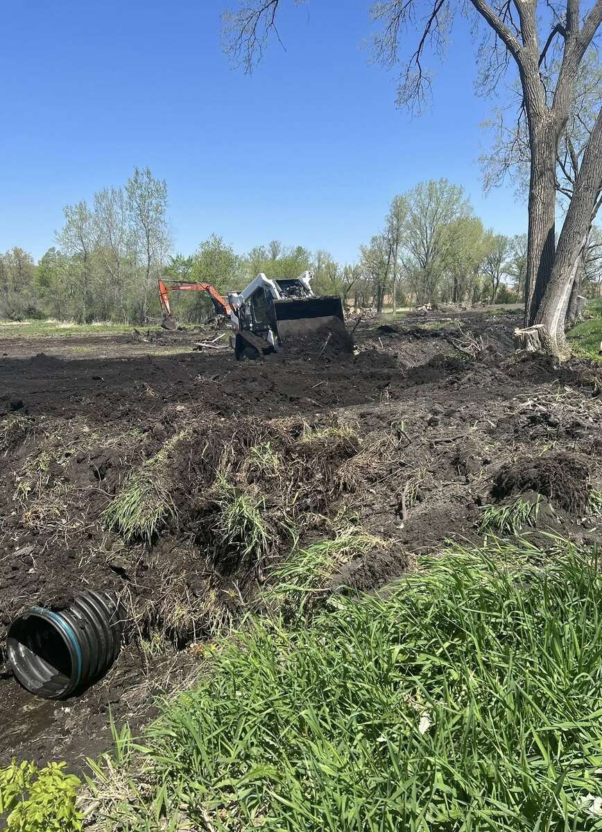 Skid steer and compact excavator on graded soil next to a black culvert pipe