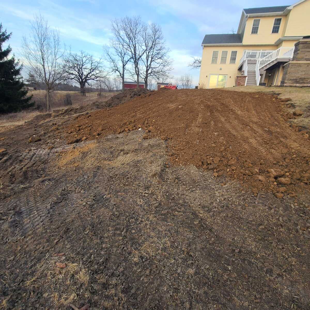 Fill dirt spread and rough graded on a hillside yard, with equipment tracks in the soil