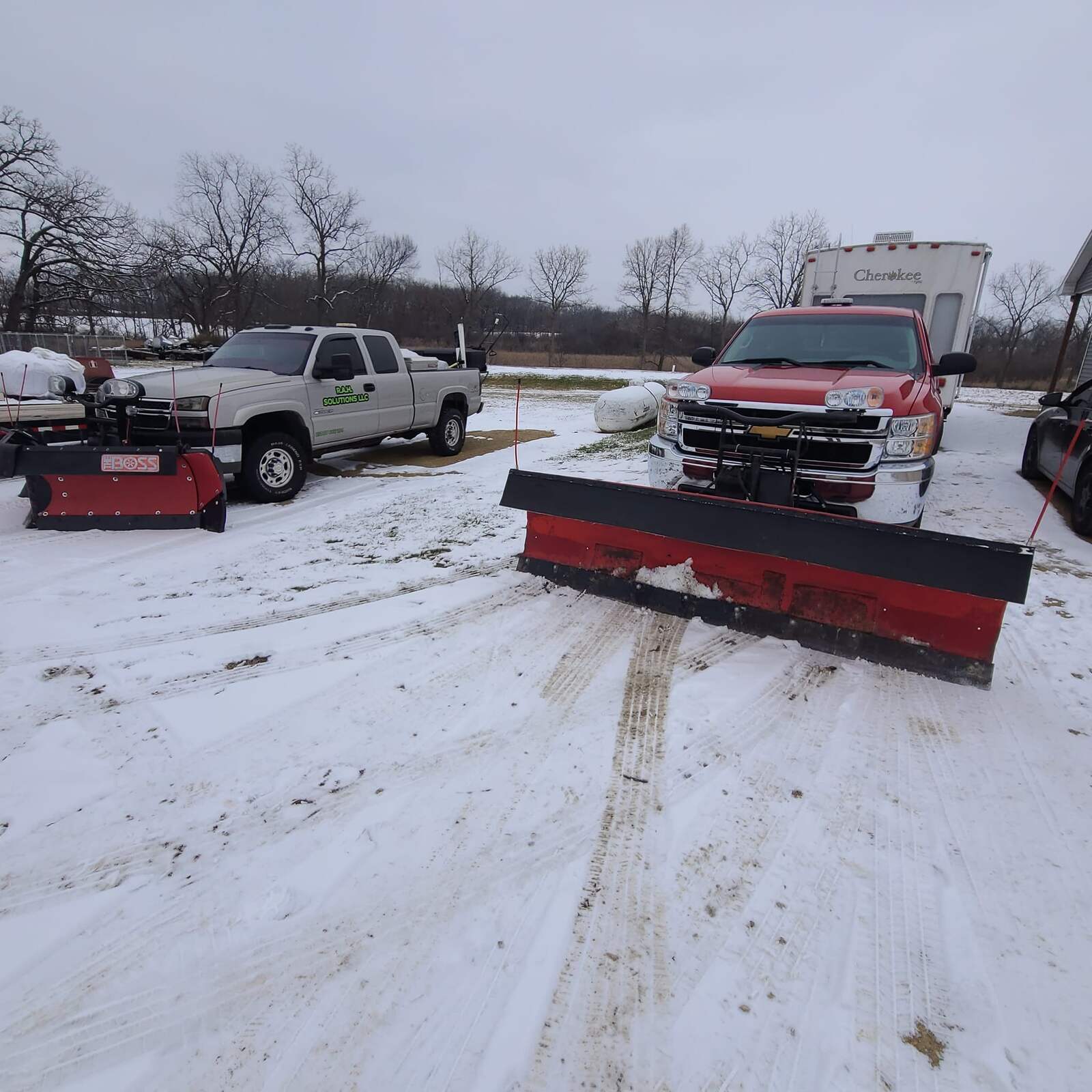 Two RAH Solutions pickup trucks with snow plows mounted on a snowy lot