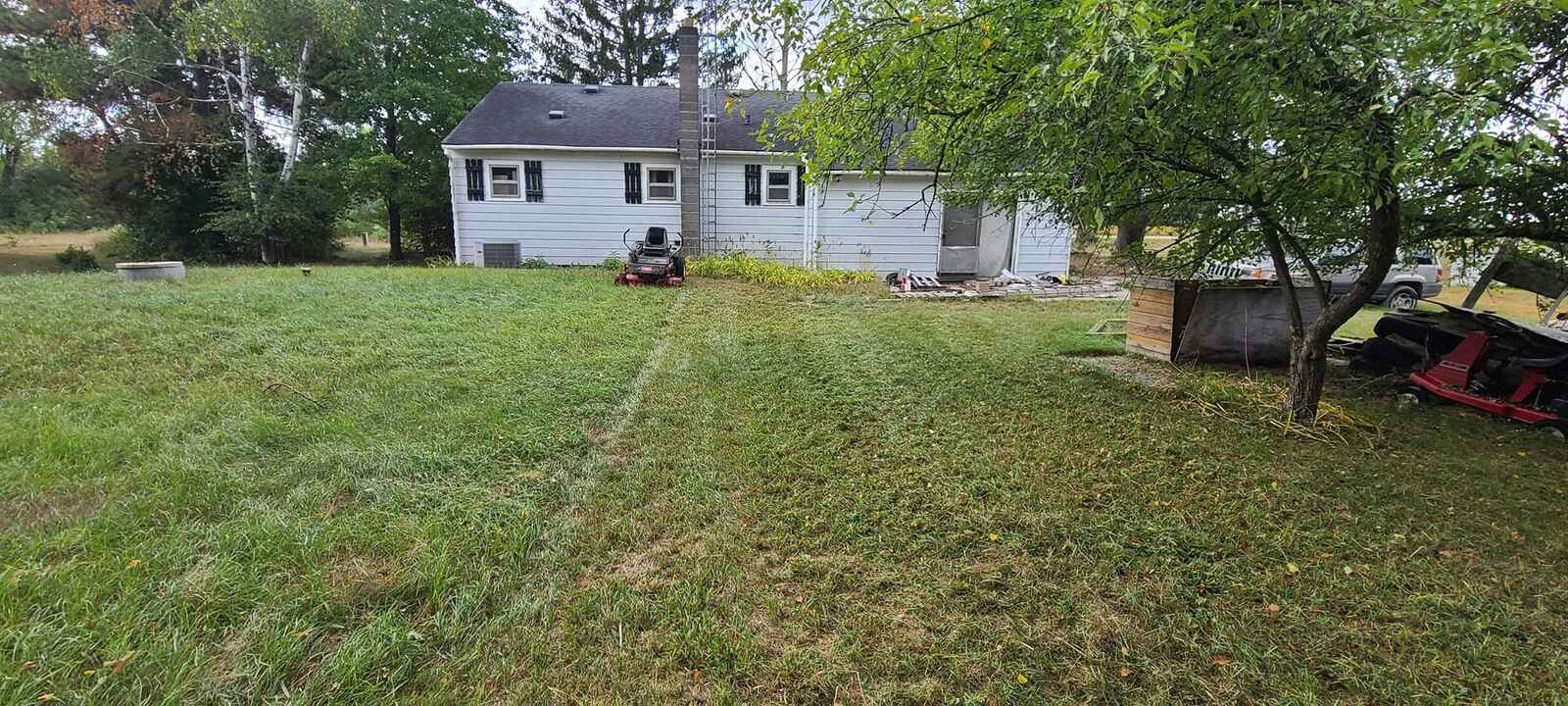 Wide mowed yard with a zero-turn mower parked near a white house